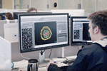 a worker sits at a computer and looks at an image of a cell on a screen.