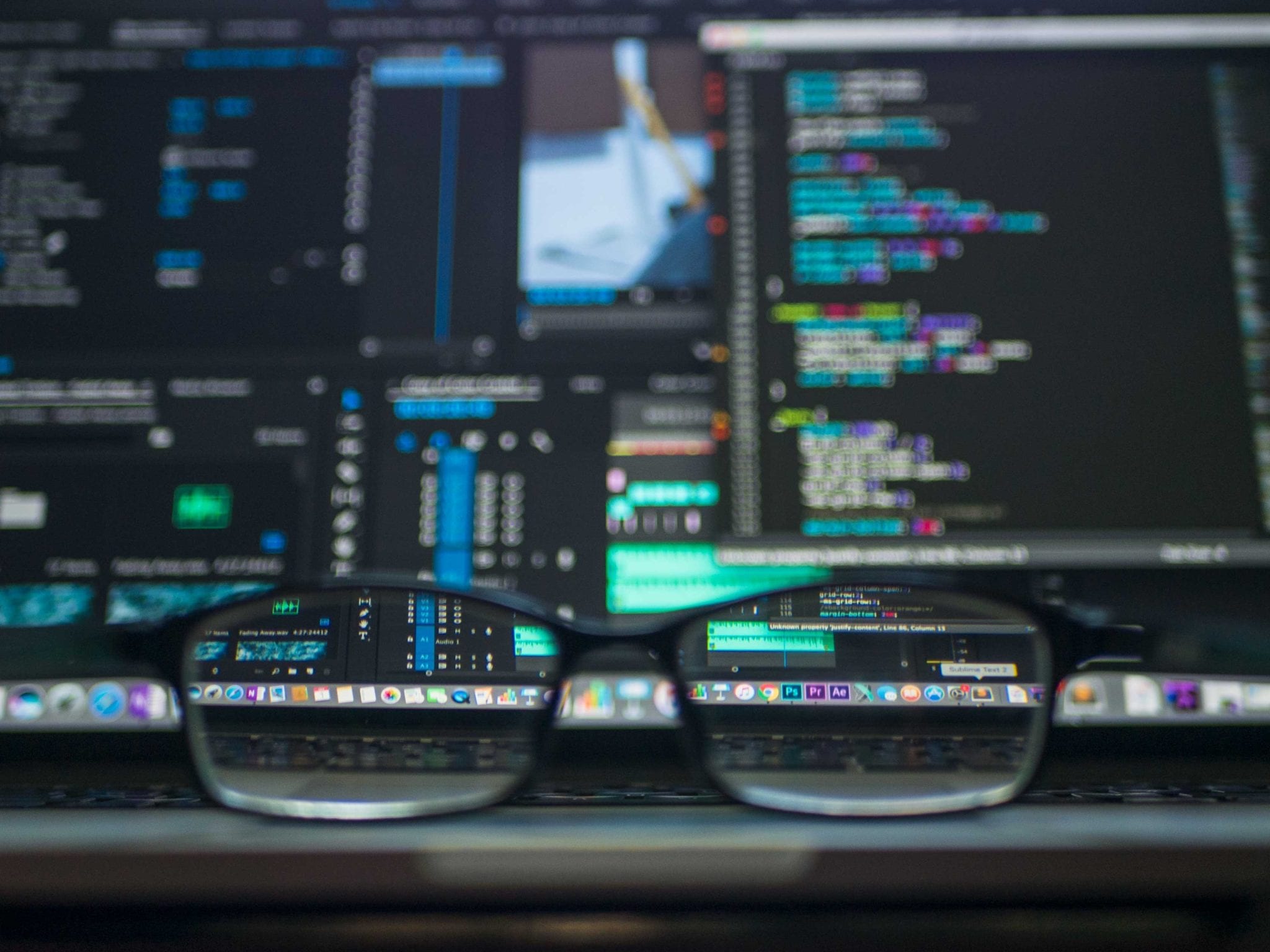 a pair of glasses sits in front of computer screens with code on them