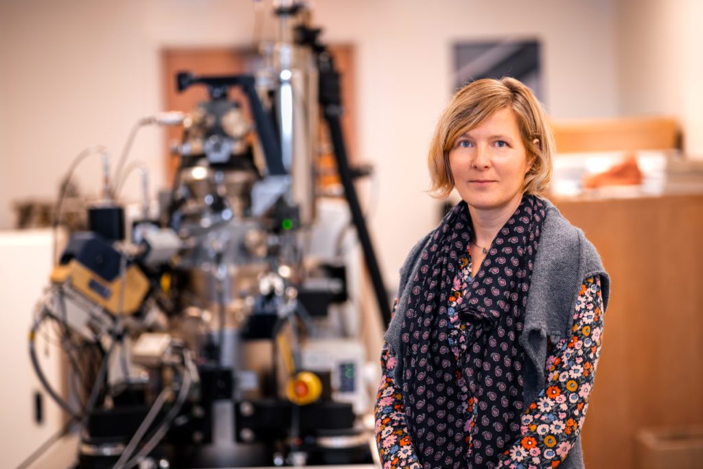 A researcher stands in front of a Zeiss ORION NanoFab.