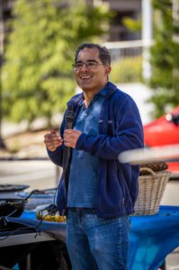 David Schaffer wearing a blue polo and fleece and holding a microphone outdoors in front of Stanley Hall