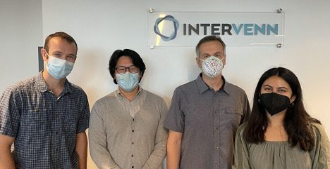 Four people in masks stand in front of a white wall with a sign that reads InterVenn Biosciences.