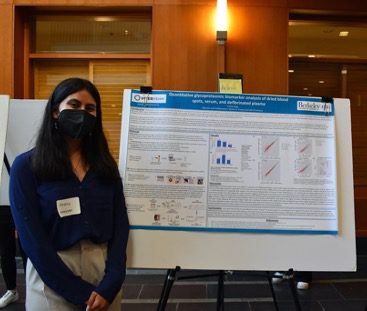 A student wearing a mask stands in front of a scientific poster