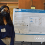 A student in a mask stands in front of a scientific poster.