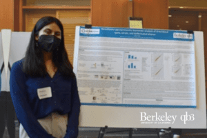 A student in a mask stands in front of a scientific poster.