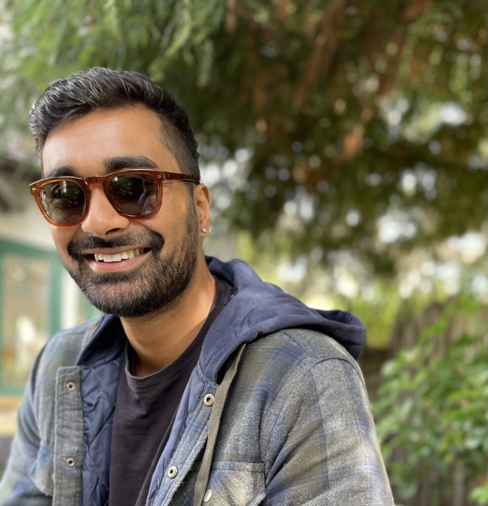Headshot of Amogh Changavi in sunglasses and a jacket in front of trees. 