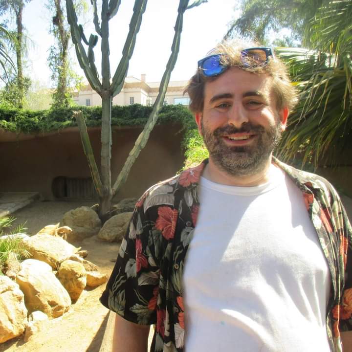 Headshot of Brian Lavin in sunglasses and a white tee shirt standing outside in front of brown rocks.