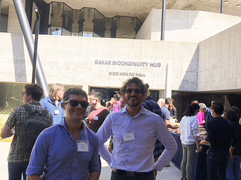 Two people wearing nametags standing in a crowd outside the Bakar Bioenginuity Hub. 
