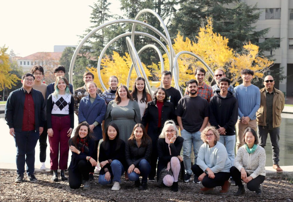 Group shot of the Nogales lab with members standing in front of the sculpture in Hearst Mining Circle. 