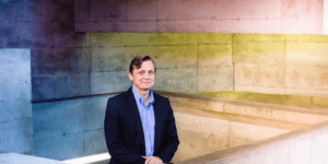 Michael Rapé standing in front of concrete highlighted by multicolored lights.