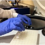 A pair of gloved hands performs RNA sample extraction in the centrifuge.