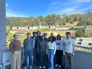 A group of people from the Lucas lab stand outside in front of a blue sky and green hills.